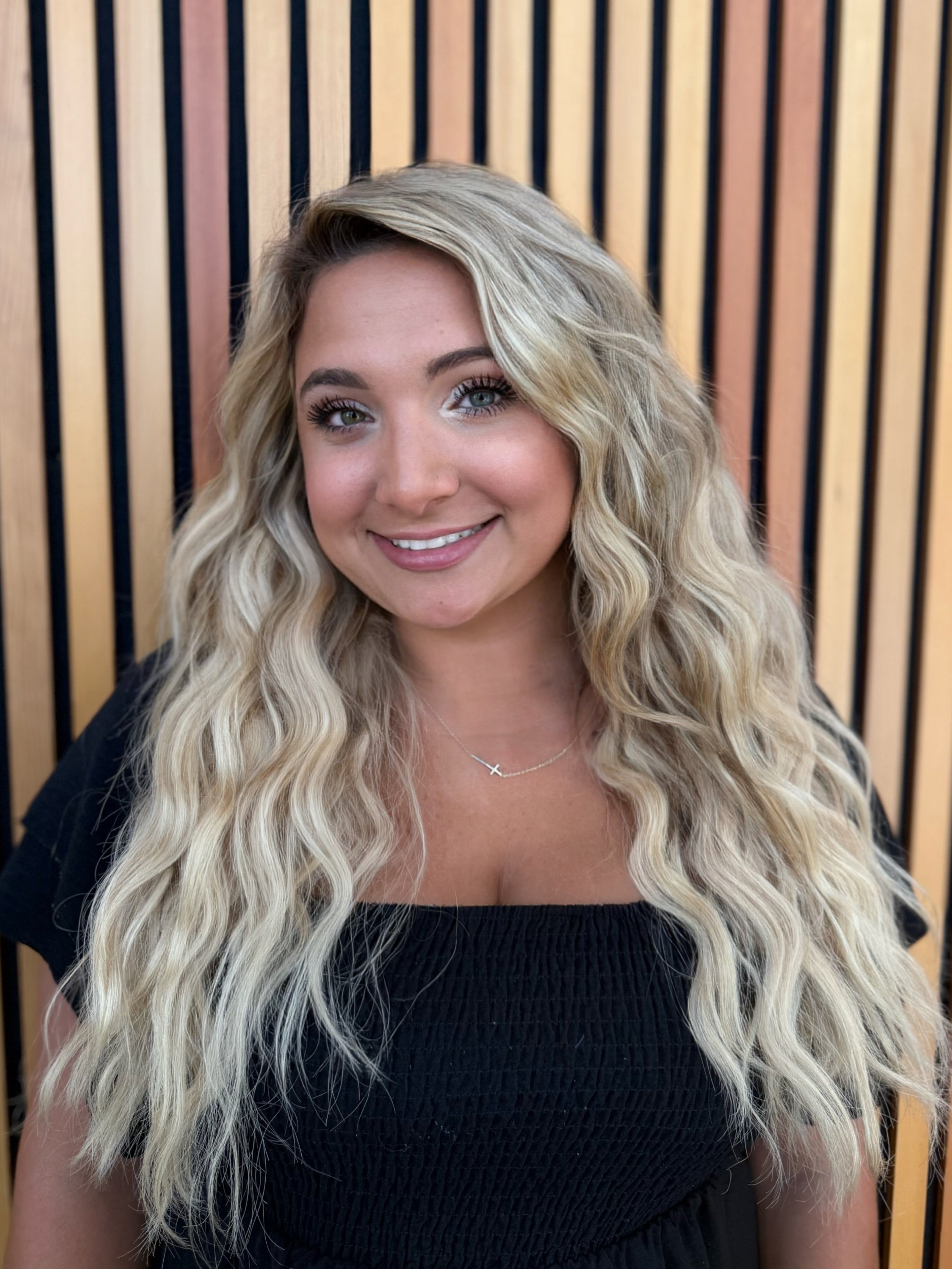 Woman with long blonde hair smiling in front of a striped wall.