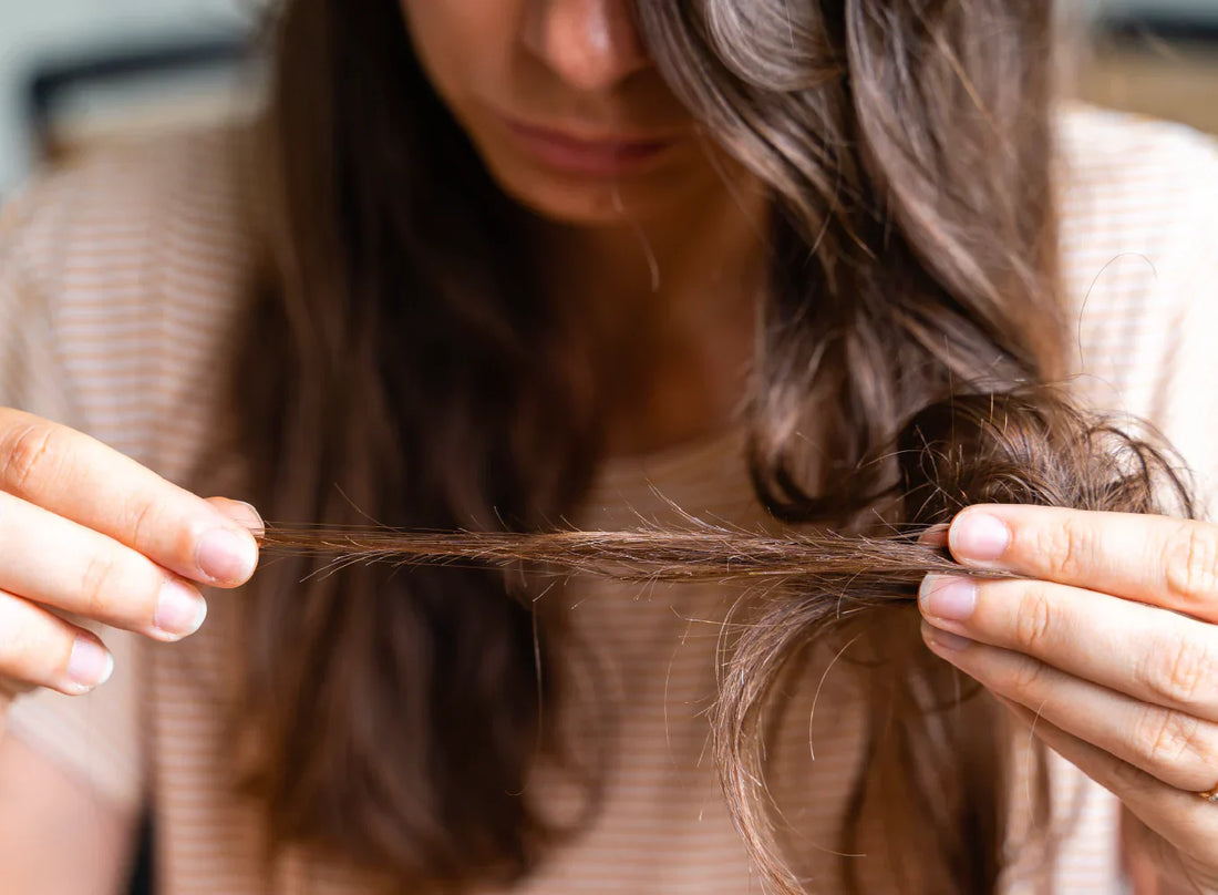 A woman looking at the split ends strands of her long brown hair