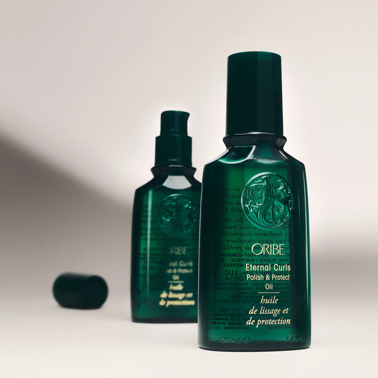 Two green bottles of Oribe Eternal Curls Oil on a light gray background