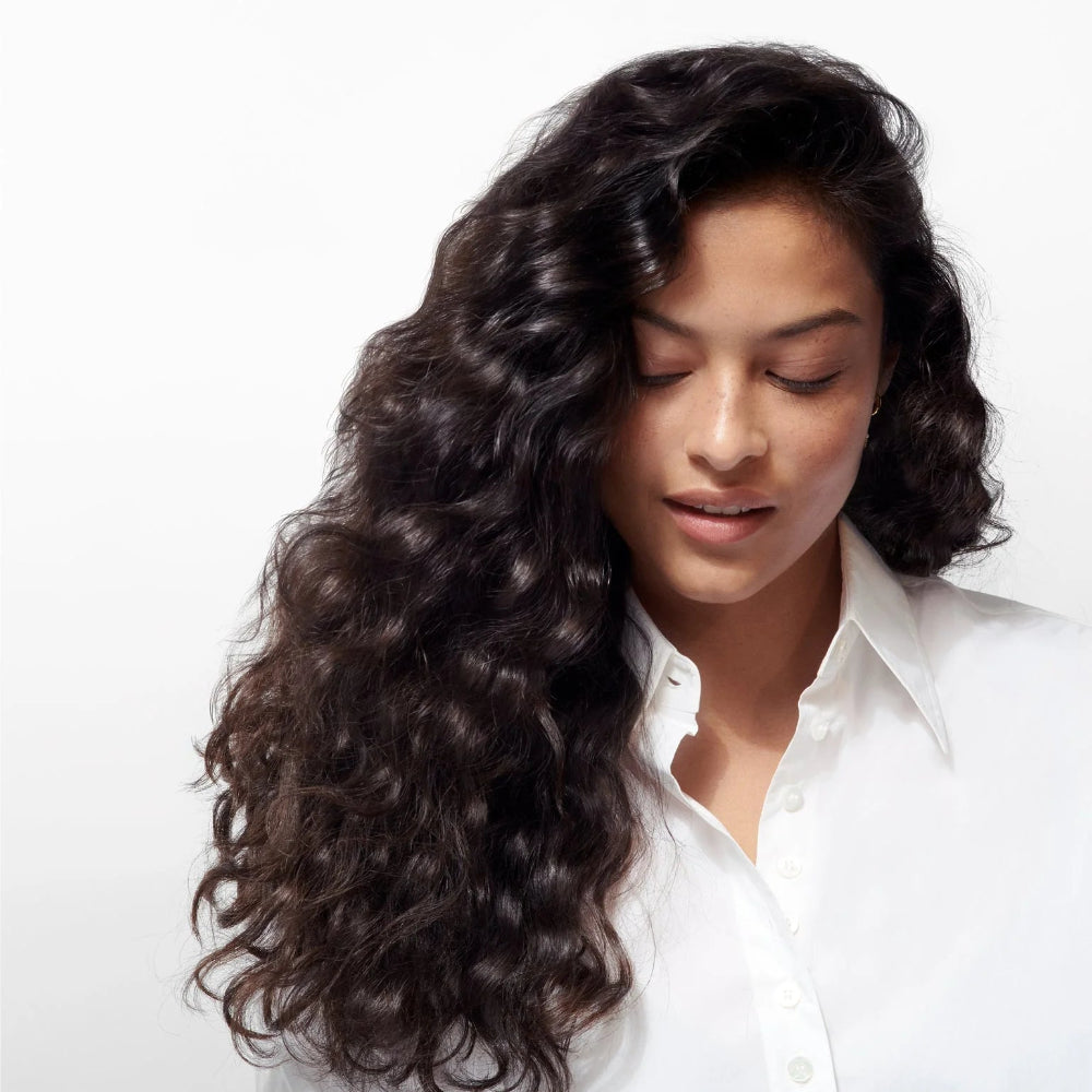 Model with long, glossy, healthy dark hair showcasing smooth, restored shine from using Oribe Gold Lust products