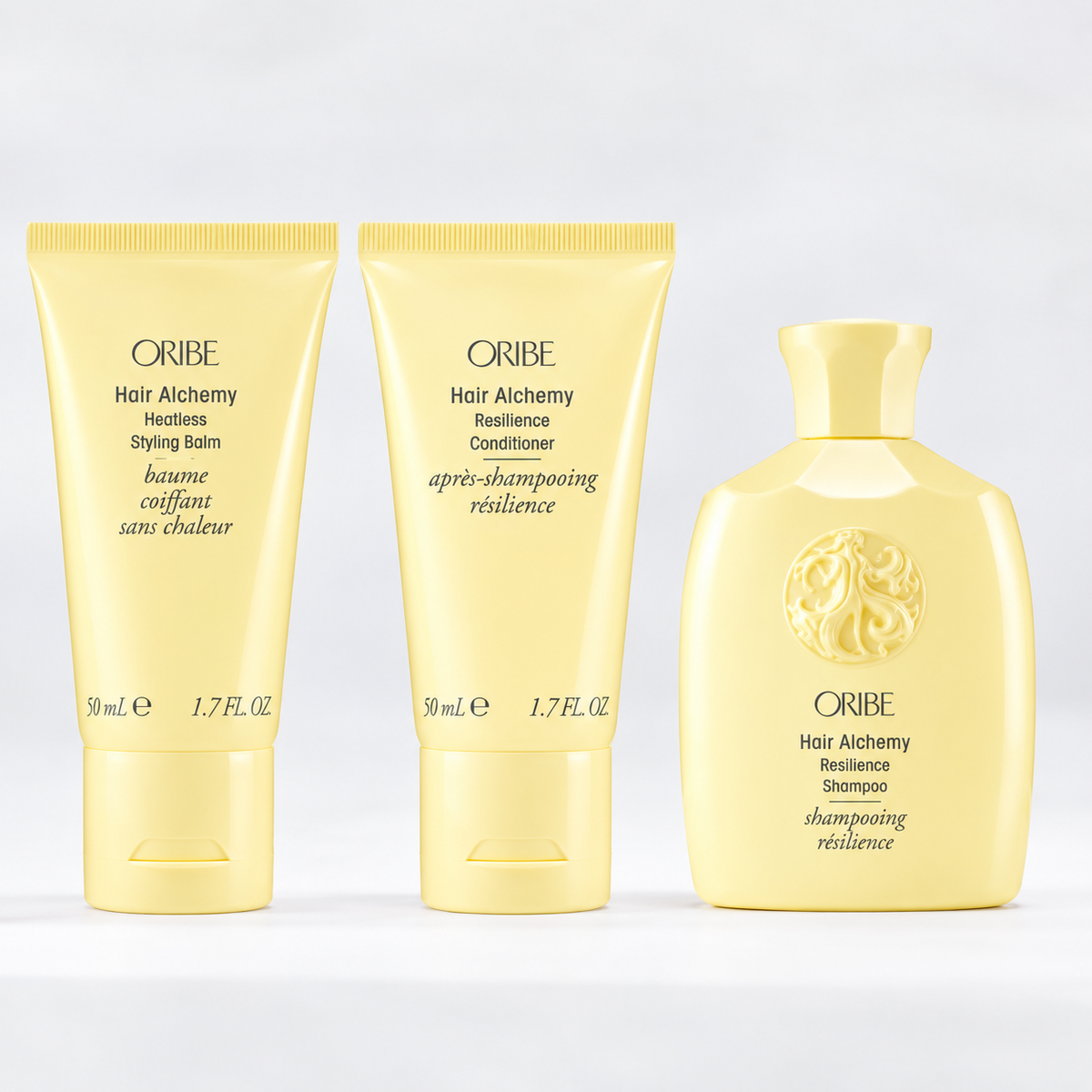 Oribe Hair Alchemy Resilience Shampoo, Conditioner, and Heatless Styling Balm in travel-size yellow packaging, a strengthening hair care trio for cleansing, conditioning, and heatless styling.
