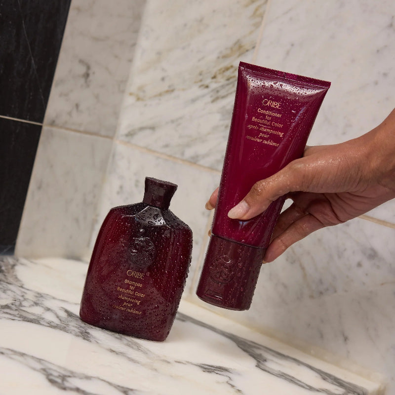 Oribe Beautiful Color shampoo bottle and conditioner tube on a marble surface