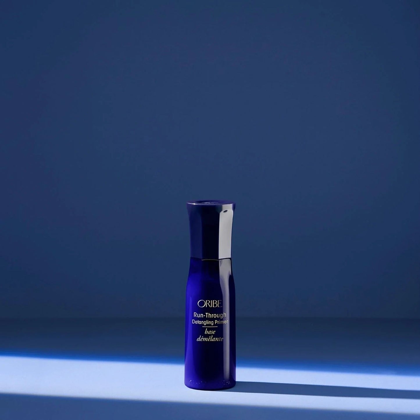Oribe Run-Through Detangling Spray Travel size standing on blue background for lightweight leave-in conditioning