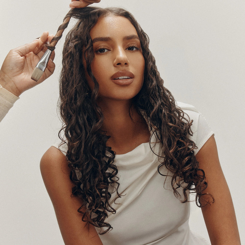 model applying Oribe curl styling product to enhance natural curls and improve definition and shine