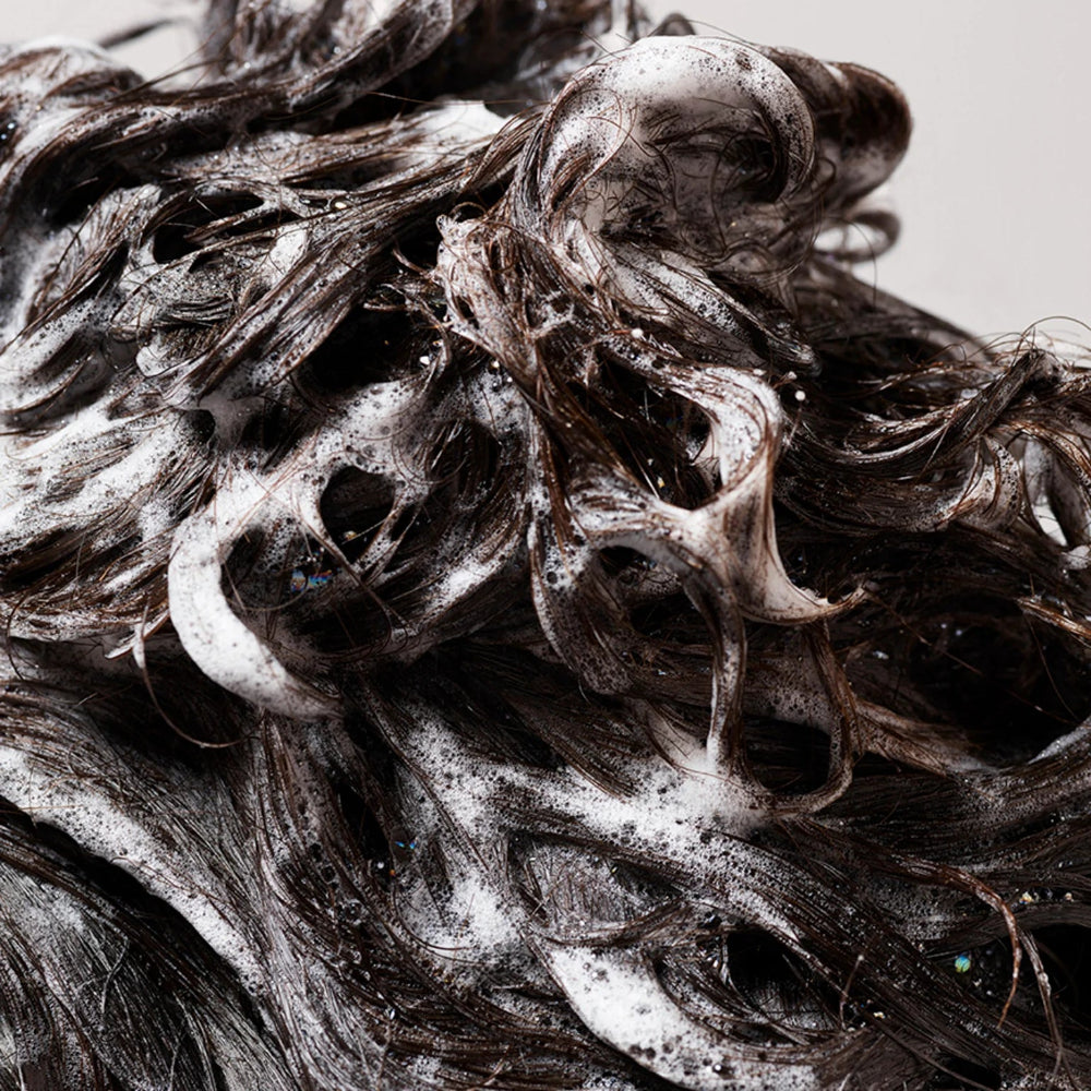Close-up of dark hair lathered with shampoo highlighting moisture and richness of Oribe Gold Lust Shampoo