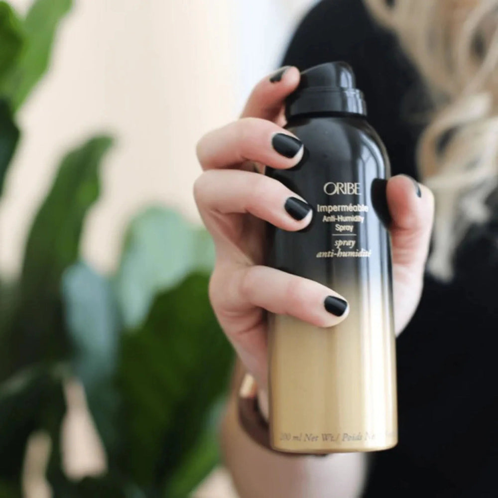 Hand holding Oribe anti-humidity spray for frizz control and smooth styling