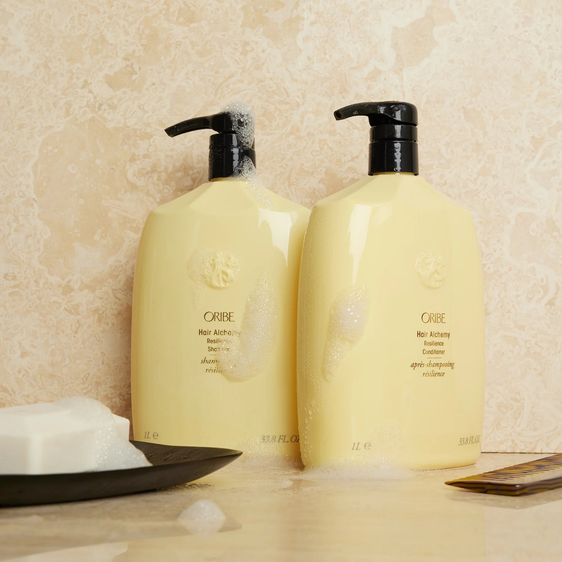 Oribe Hair Alchemy shampoo and conditioner bottles displayed in bathroom setting for damaged hair repair