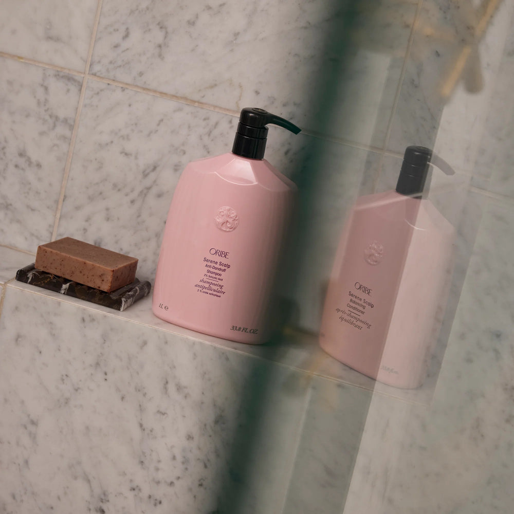 Oribe Serene Scalp shampoo and conditioner bottles on shower shelf for complete scalp care routine