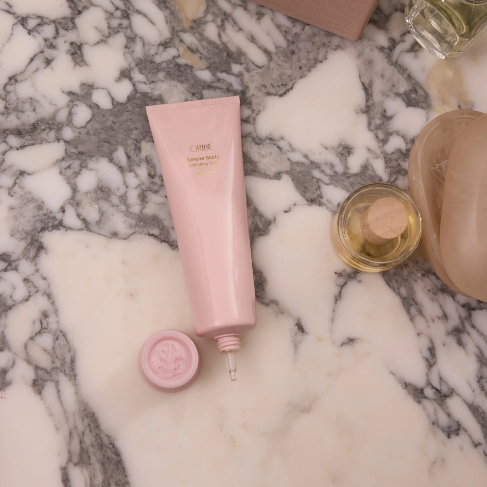 Oribe Serene Scalp exfoliating scrub tube displayed with luxury hair care products on marble surface